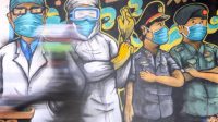 Pengendara melintas di depan mural tentang pandemi COVID-19 di Kawasan Bangil, Pasuruan, Sidoarjo, Jawa Timur. (Foto: ANTARA FOTO Umarul Faruq)