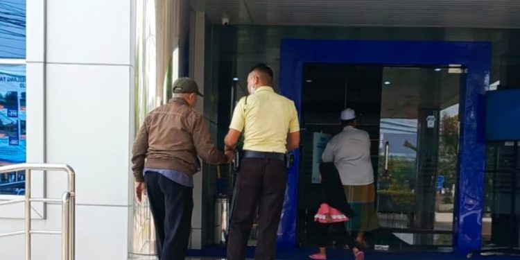 Satpam BRI Cabang Purworejo dengan sabar membantu nasabahnya masuk ke dalam Bank BRI