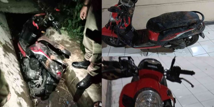 sepeda motor Scoopy warna merah hitam yang tertinggal di saluran irigasi di Ring Road Manding