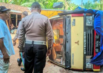 Petugas kepolisian bersama warga berada di lokasi kecelakaan truk Mitsubishi Colt Diesel bernomor polisi AB 8494 GC yang terguling di Jalan Wates–Sermo, Pengasih, Kulon Progo