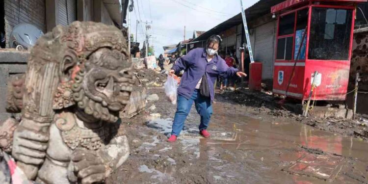 Warga berjalan melewati lumpur pascabanjir di Pasar Kumbasari, Denpasar, Bali