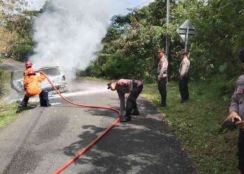 Petugas Damkar Kulonprogo bersama aparat kepolisian berupaya memadamkan api yang membakar mobil Grand Livina di Jalan Raya Kiskendo, Giripurwo, Girimulyo