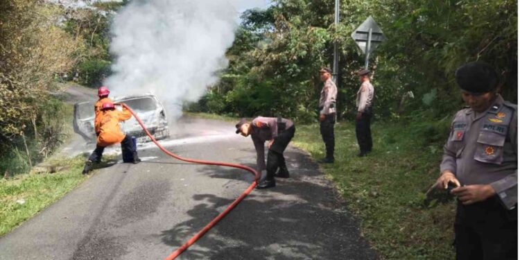 Petugas Damkar Kulonprogo bersama aparat kepolisian berupaya memadamkan api yang membakar mobil Grand Livina di Jalan Raya Kiskendo, Giripurwo, Girimulyo
