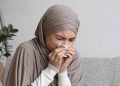 Seorang perempuan tampak bersin sambil menutup hidung dengan tisu, menggambarkan kondisi orang yang sedang kurang sehat dan membutuhkan doa serta dukungan. Dalam Islam, ungkapan syafakillah kerap disampaikan sebagai doa agar Allah memberikan kesembuhan, ketenangan, dan perlindungan bagi yang sedang sakit.