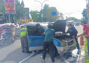 Petugas kepolisian bersama warga membantu memadamkan api pada mobil Hyundai Atos yang sempat mengeluarkan asap dan terbakar di Perempatan Traffic Light Condongcatur, Kapanewon Depok, Sleman, Rabu (7/1/2026).