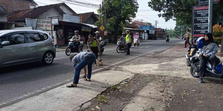 Petugas kepolisian bersama warga membersihkan sisa material di lokasi kecelakaan lalu lintas di Jalan Imogiri Timur, tepatnya di depan SMKN 1 Pleret, Bantul
