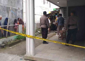 Petugas kepolisian memasang garis polisi di lokasi penemuan seorang pria yang meninggal dunia di rumah kontrakan wilayah Bangunharjo, Sewon, Bantul, Senin (9/2/2026) pagi. Sejumlah warga tampak menyaksikan proses olah tempat kejadian perkara yang dilakukan aparat bersama tim medis.