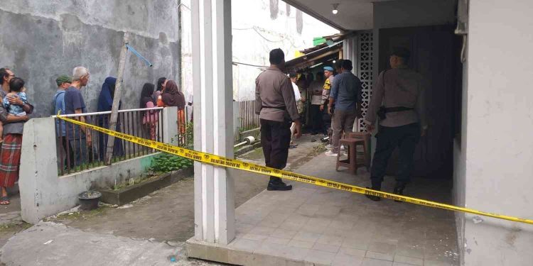 Petugas kepolisian memasang garis polisi di lokasi penemuan seorang pria yang meninggal dunia di rumah kontrakan wilayah Bangunharjo, Sewon, Bantul, Senin (9/2/2026) pagi. Sejumlah warga tampak menyaksikan proses olah tempat kejadian perkara yang dilakukan aparat bersama tim medis.