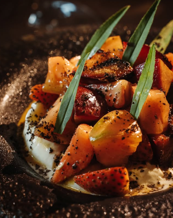Salad burrata dengan plum panggang dan stroberi yang disajikan di atas piring batu vulkanik